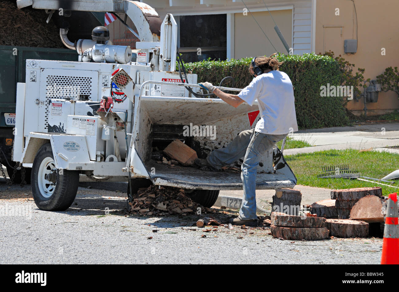 worker trying to kick wood into a chipper in an unsafe and unprotected way (how not to use a wood chipper) Stock Photo