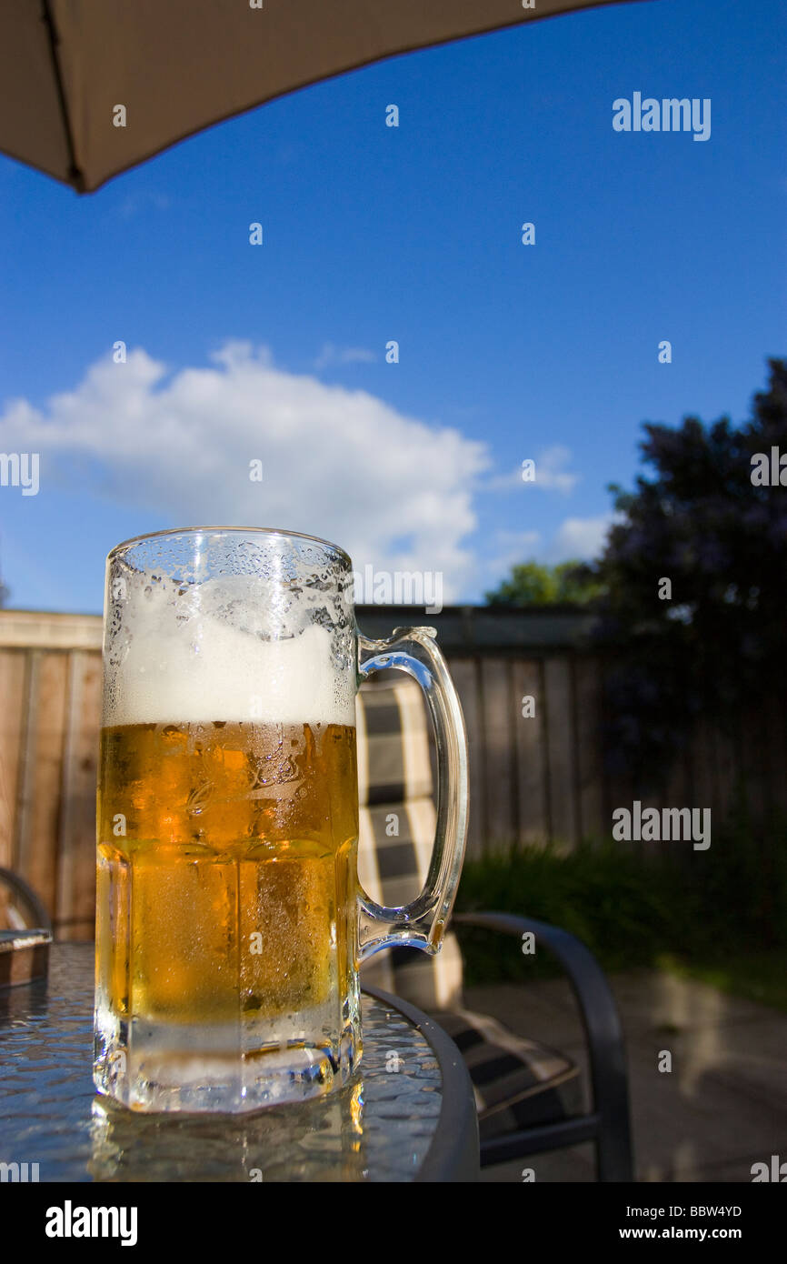 Cold beer in glass with frothy head in sunshine atop a patio table during bbq Stock Photo