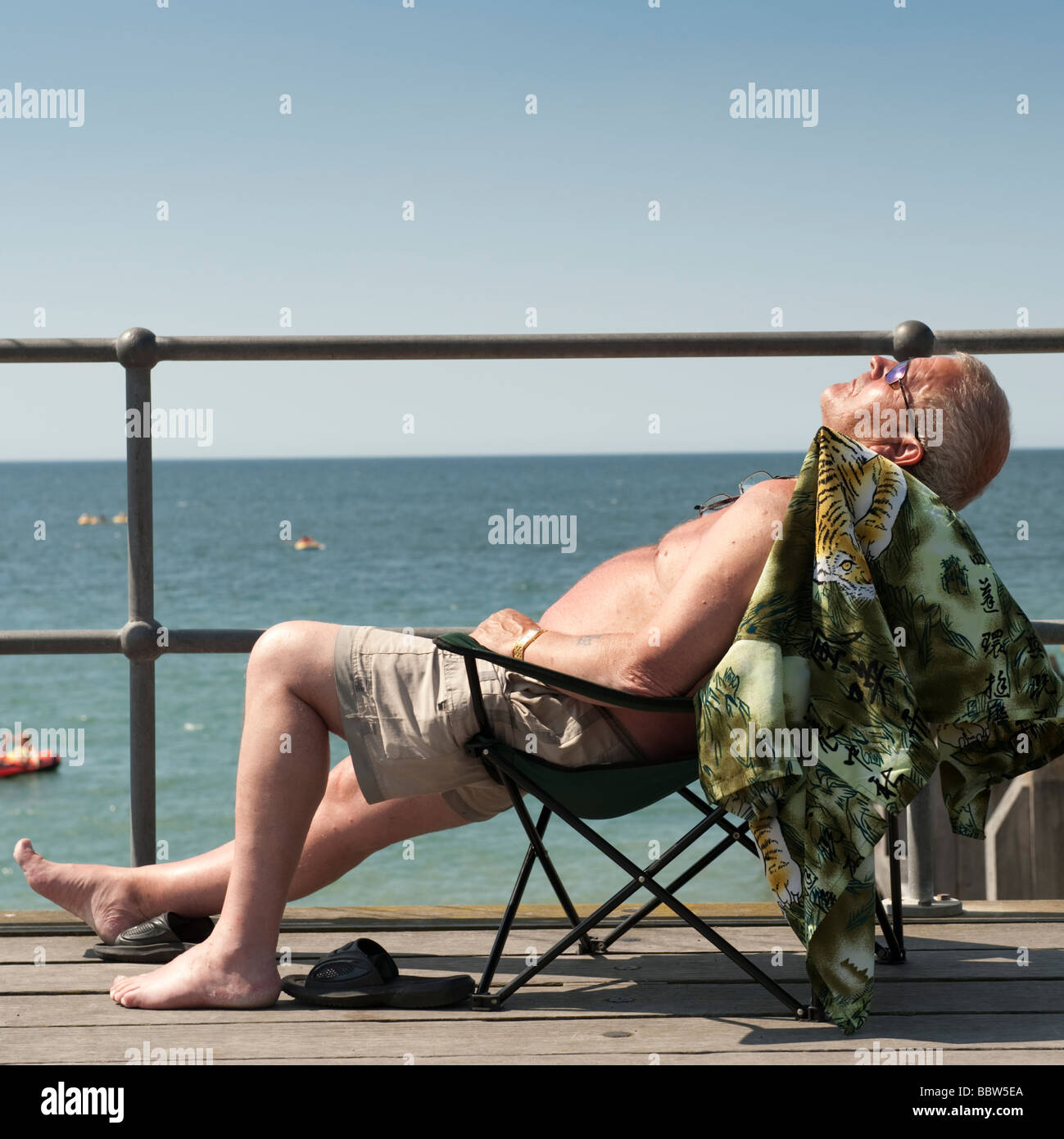 A middle aged man sitting in a folding chair sunbathing Aberystwyth promenade Wales UK Stock Photo