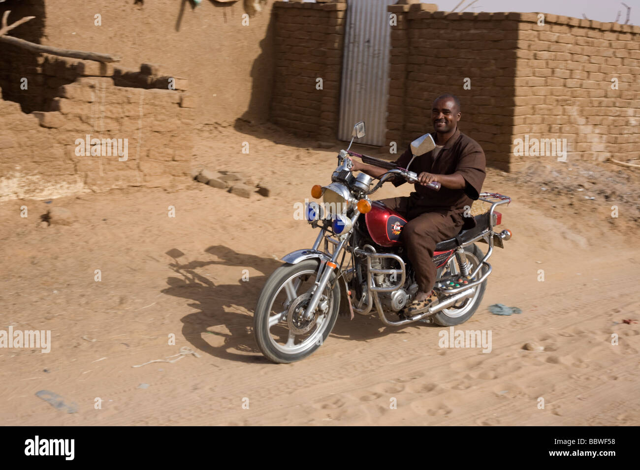 Man on a smart motorbike smiles as he rides past the viewer in the 4 sq km Abu Shouk refugee camp in Al Fasher, North Darfur Stock Photo