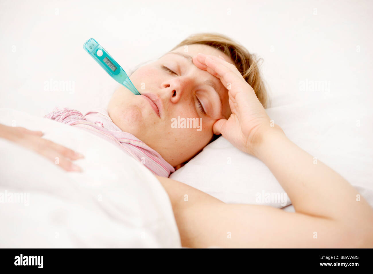 Woman at home, ill with fever in her bed, uses a clinical thermometer for measuring body temperature. Stock Photo