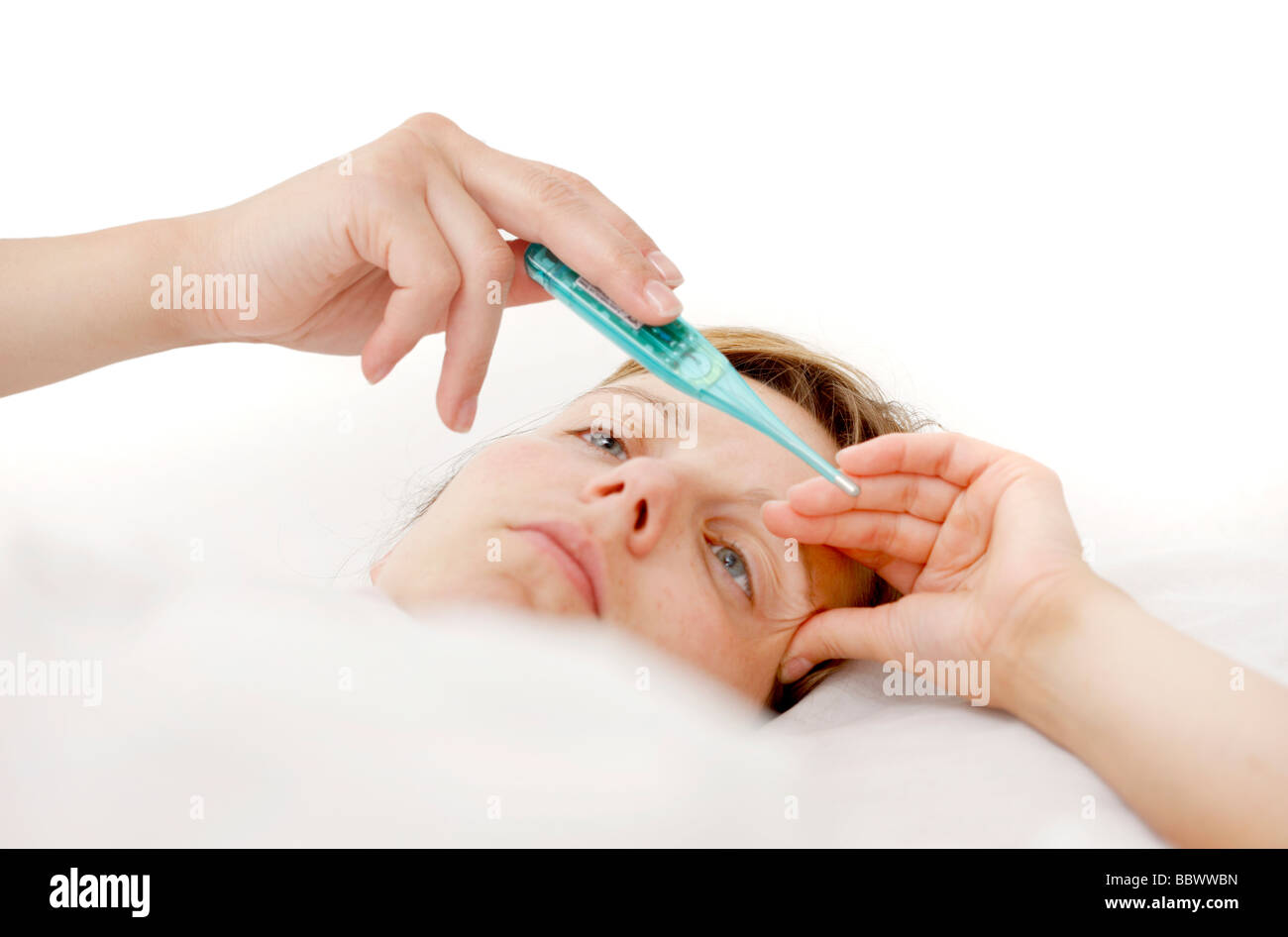 Woman at home, ill with fever in her bed, uses a clinical thermometer for measuring body temperature. Stock Photo