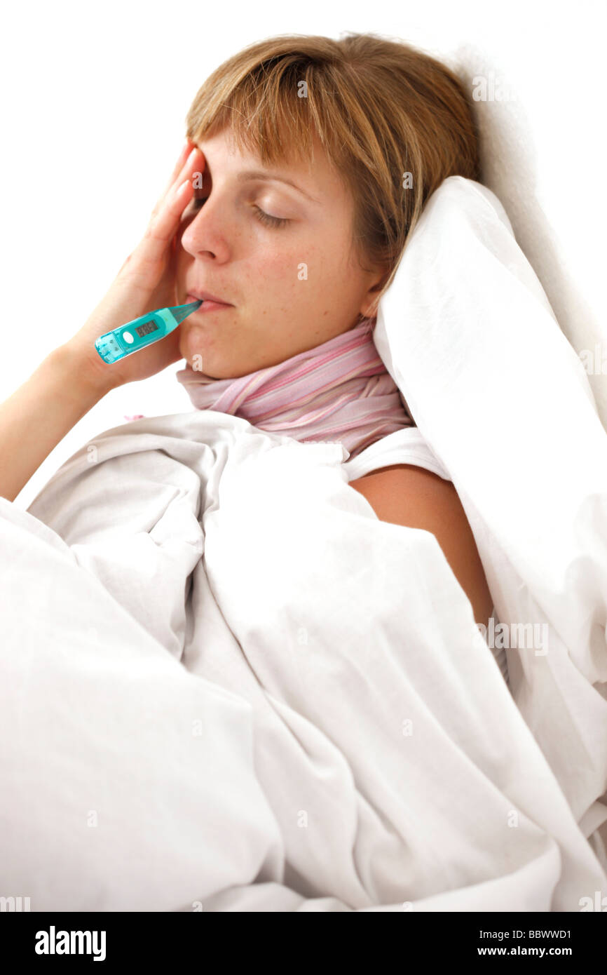 Woman at home, ill with fever in her bed, uses a clinical thermometer for measuring body temperature. Stock Photo