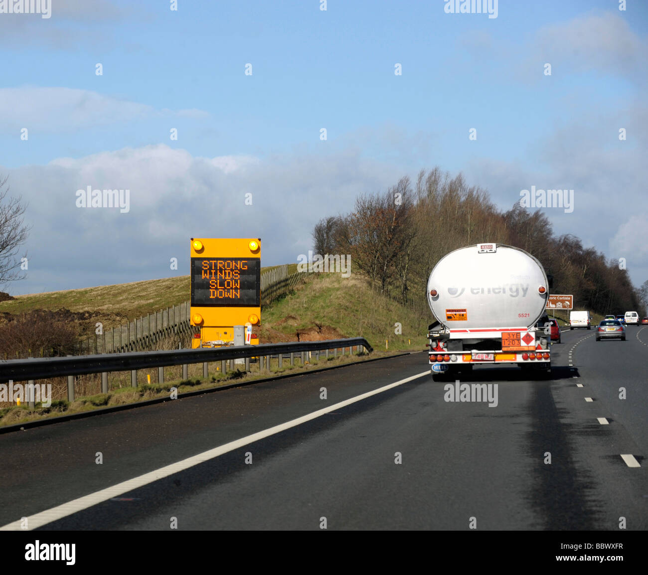 Warning matrix slow down strong winds on motorway as LGV large goods vehicle HGV fuel petrol tanker passes Stock Photo