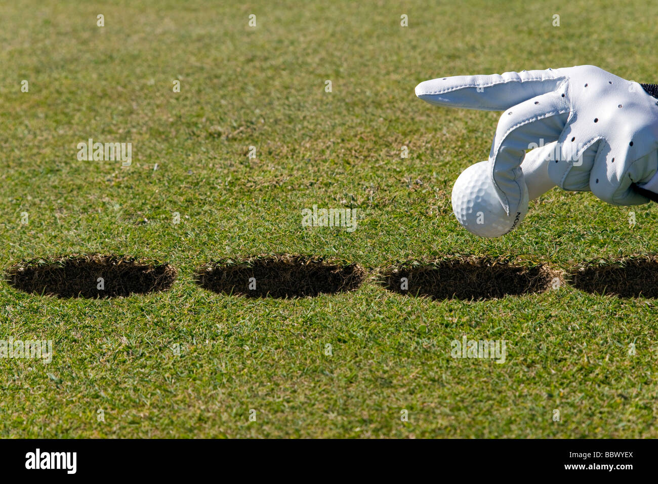 Hand holding golf ball over several holes, the other kind of putting Stock Photo