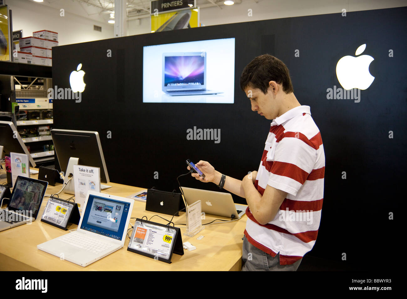 teenager examining iPhone at Apple stand in Best Buy store, USA Stock Photo