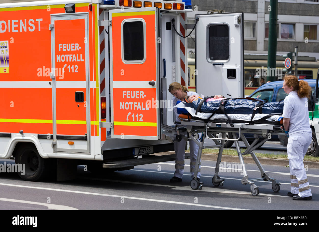 female medics carrying traffic accident victim on stretcher into ambulance car Stock Photo
