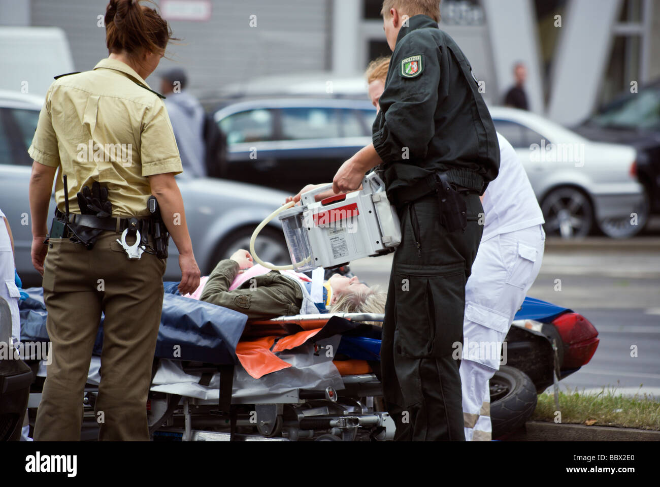 policemen helping medics at motorbike accident, injured girl on stretcher Stock Photo