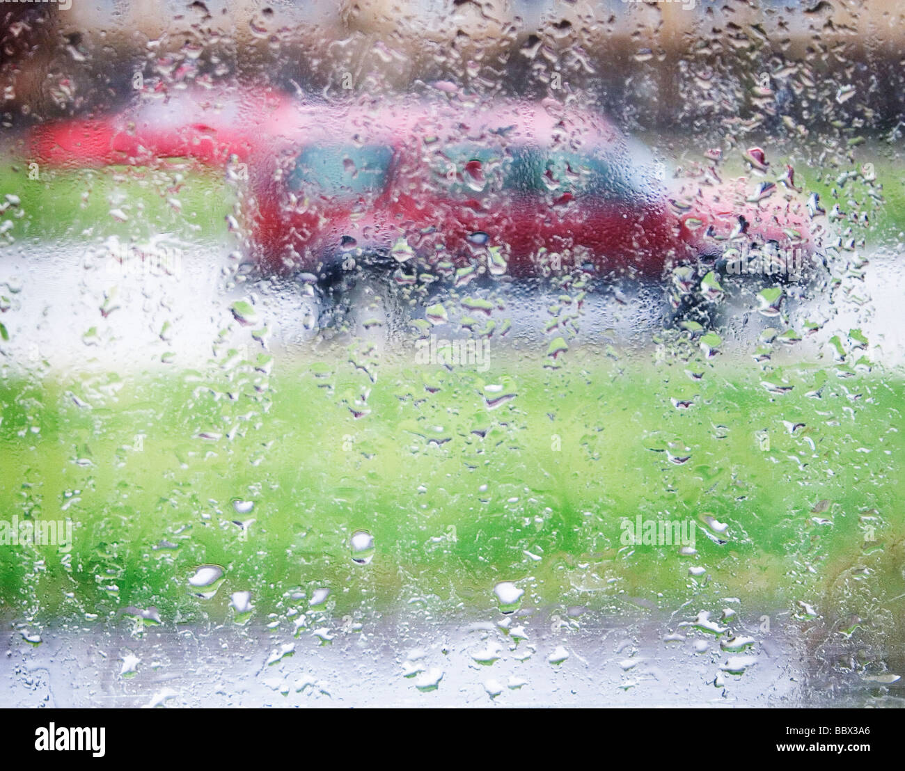 Raindrops on a window pane with a red car in the background Sweden. Stock Photo