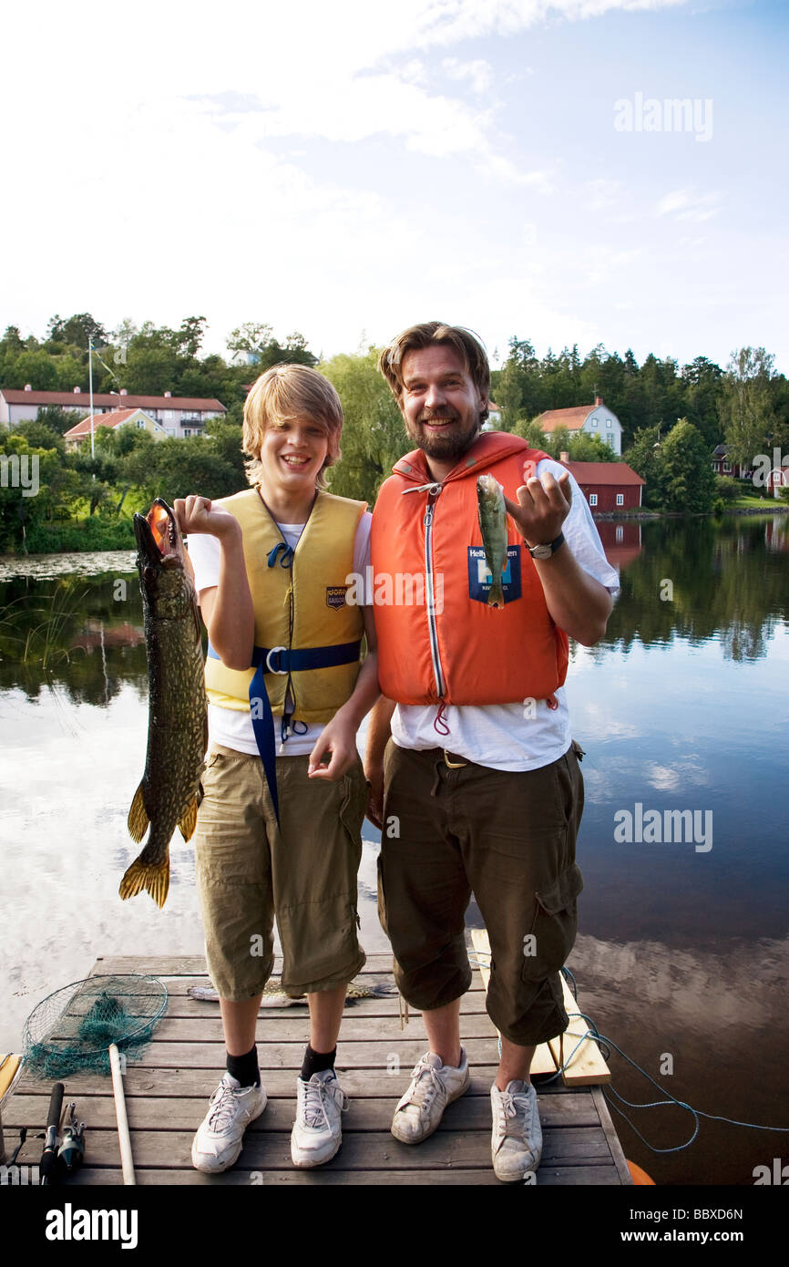 Father and son holding fishes standing on a jetty Sweden. Stock Photo