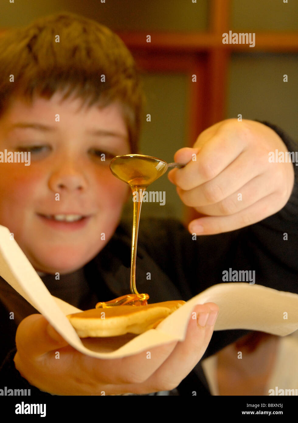 Smiling boy pours syrup onto pancake from spoon Stock Photo Alamy