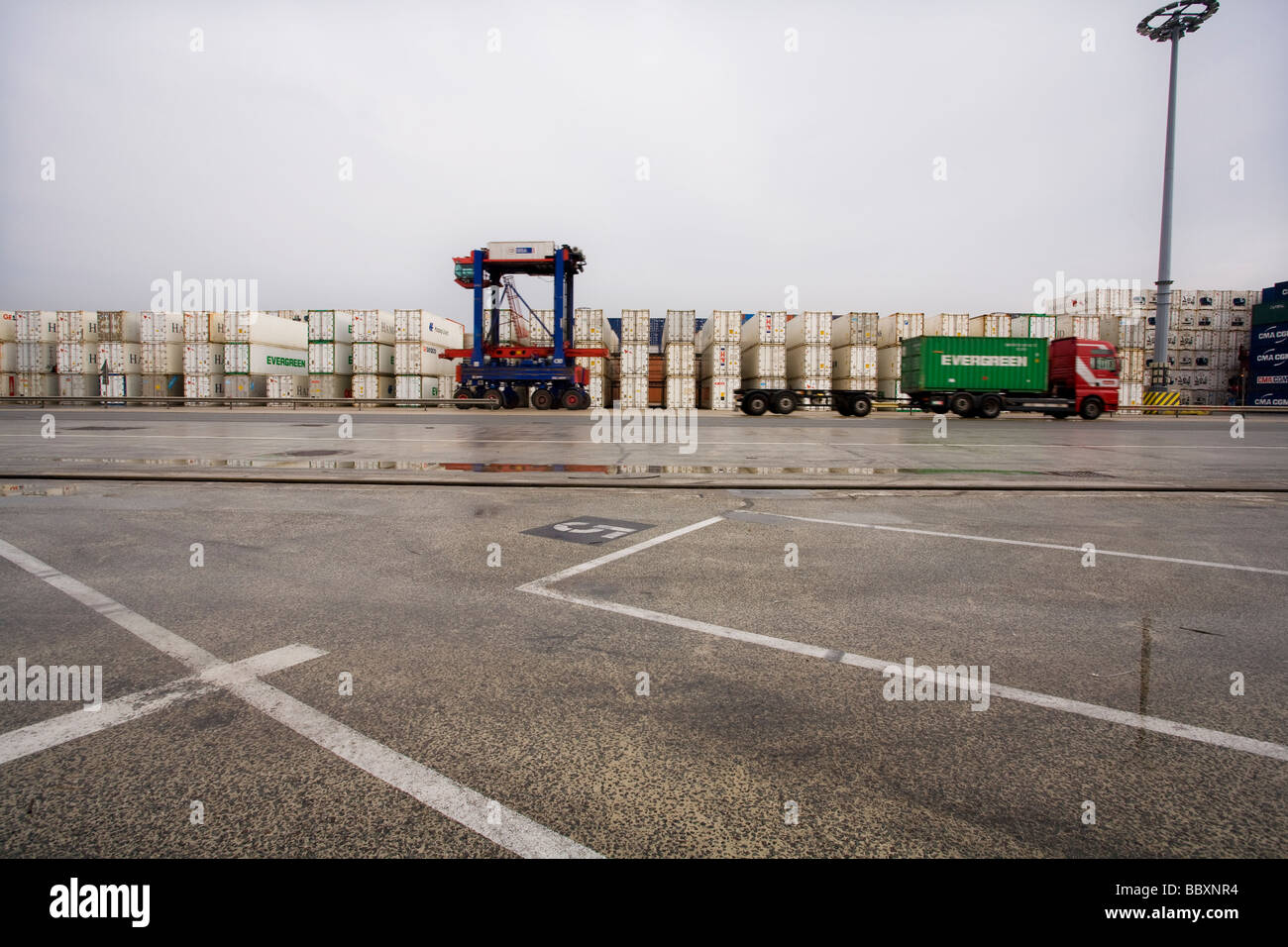 A straddle carrier and container lorry speed past a neat stack of ...