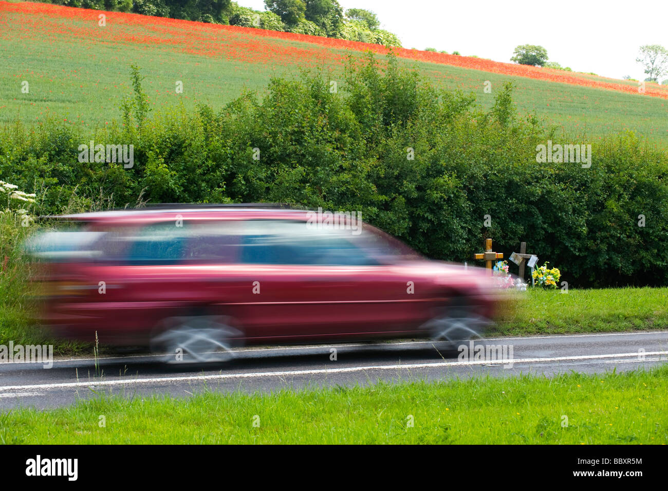 A ROAD SIDE SHRINE MARKS A PREVIOUS FATAL ROAD ACCIDENT AS A CAR SPEEDS PAST.  NEAR CHESHAM, BUCKINGHAMSHIRE, ENGLAND. Stock Photo
