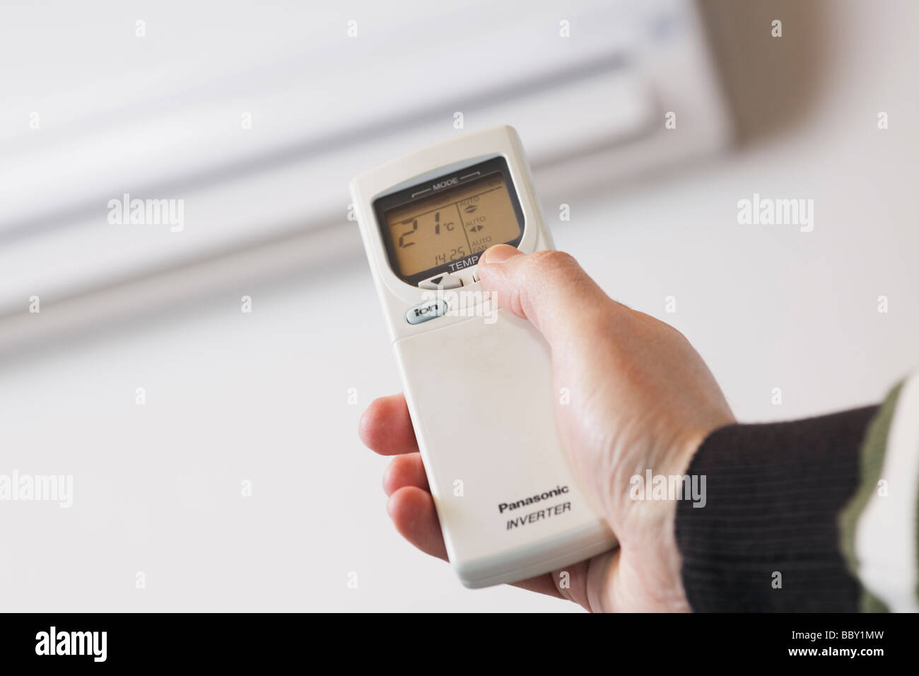 Hand using remote control of a reverse cycle air conditioner heat pump seen in background Stock Photo