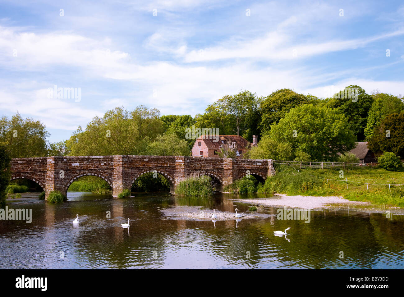 Bridge with White Mill in background with swans reflections from trees, with blue sky and fluffy clouds on summer's day, Dorset Stock Photo