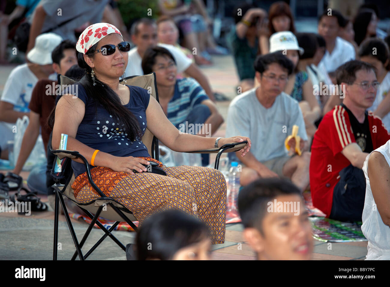 A woman seated and alone in a crowd Stock Photo