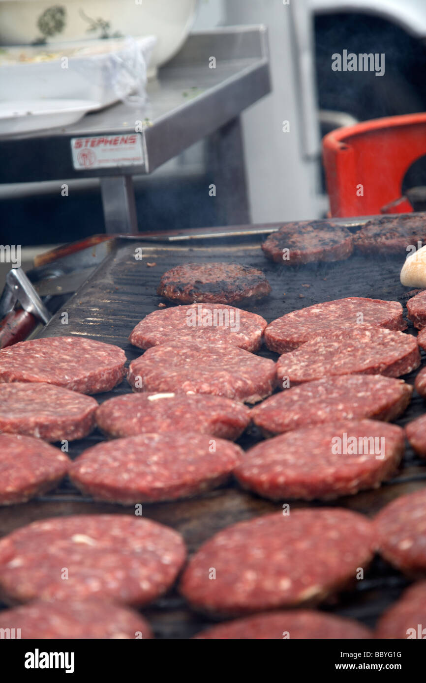 raw hamburgers being cooked on an open grill for sale at a public event county down northern ireland uk Stock Photo