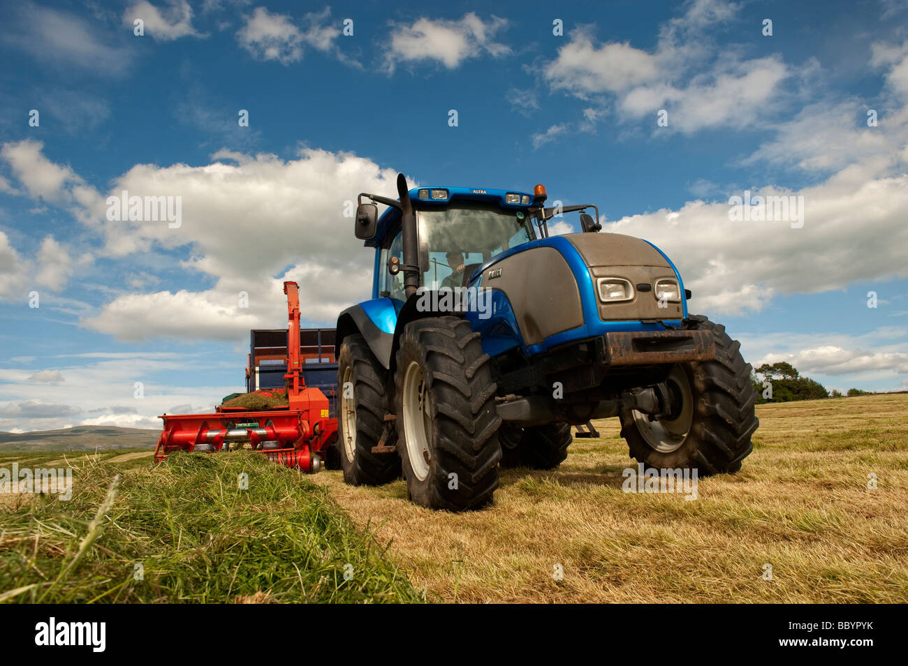 Valtra tractor pulling a Kverneland forage harvester and trailer making silage for livestock Cumbria England Stock Photo