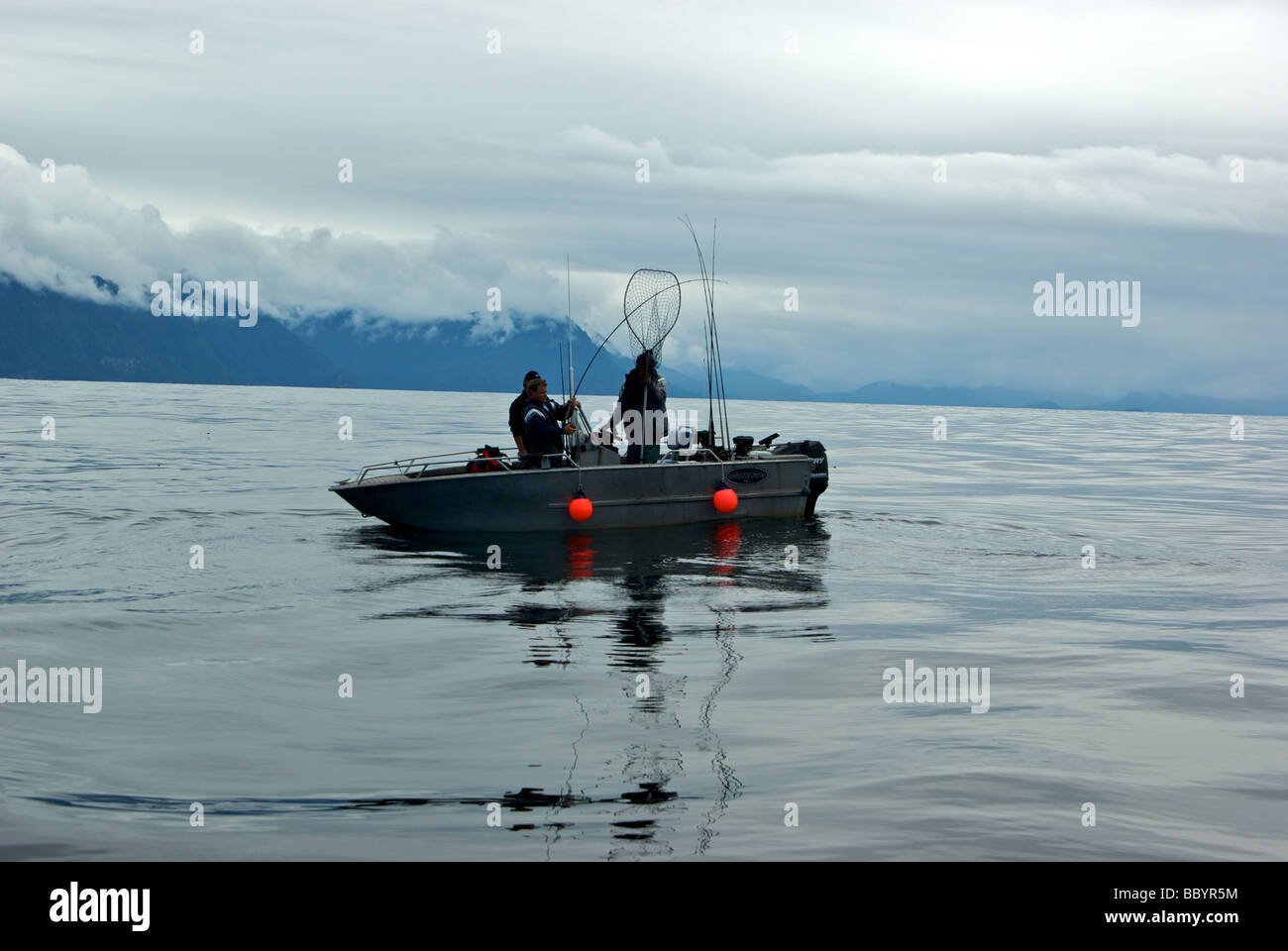 Male angler playing a chinook salmon in open Pacific Ocean at Freeman Rocks against backdrop of Graham Island Haida Gwaii Stock Photo