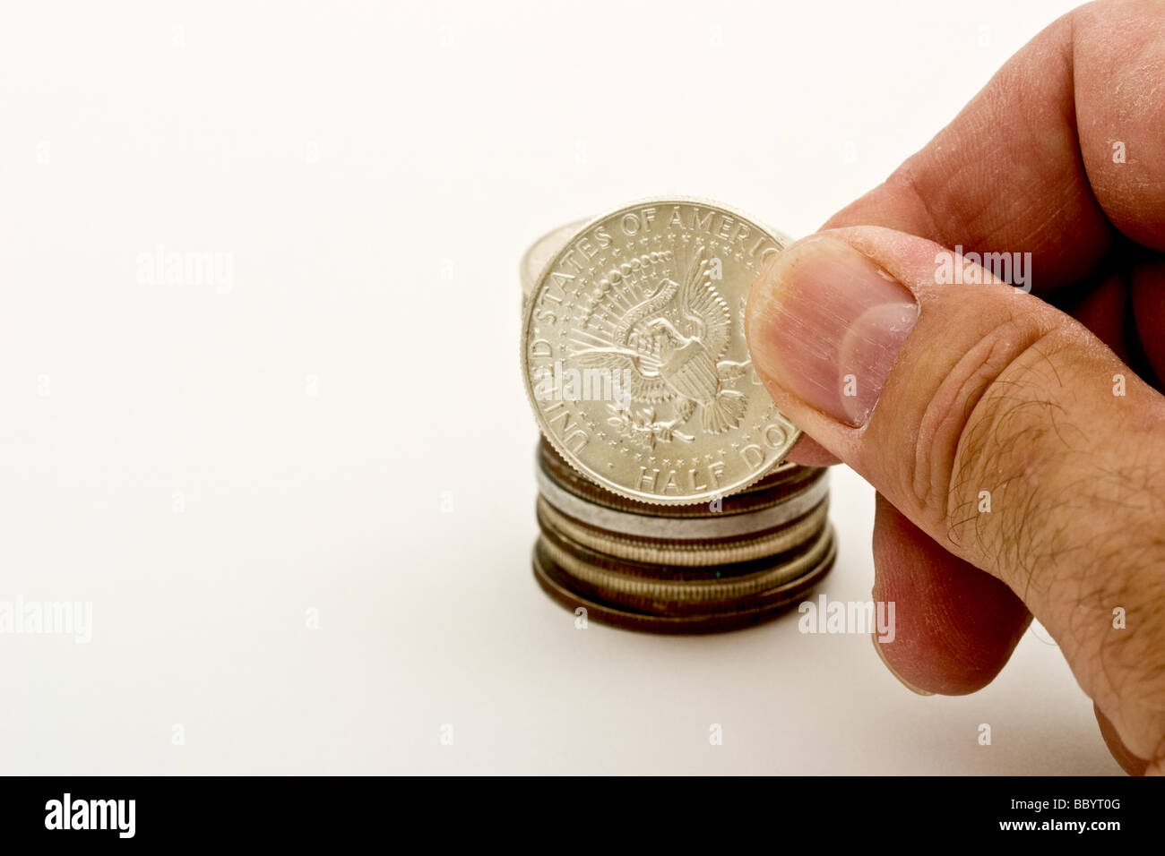 Fingers holding an American half dollar coin in front of a pile of coins Stock Photo