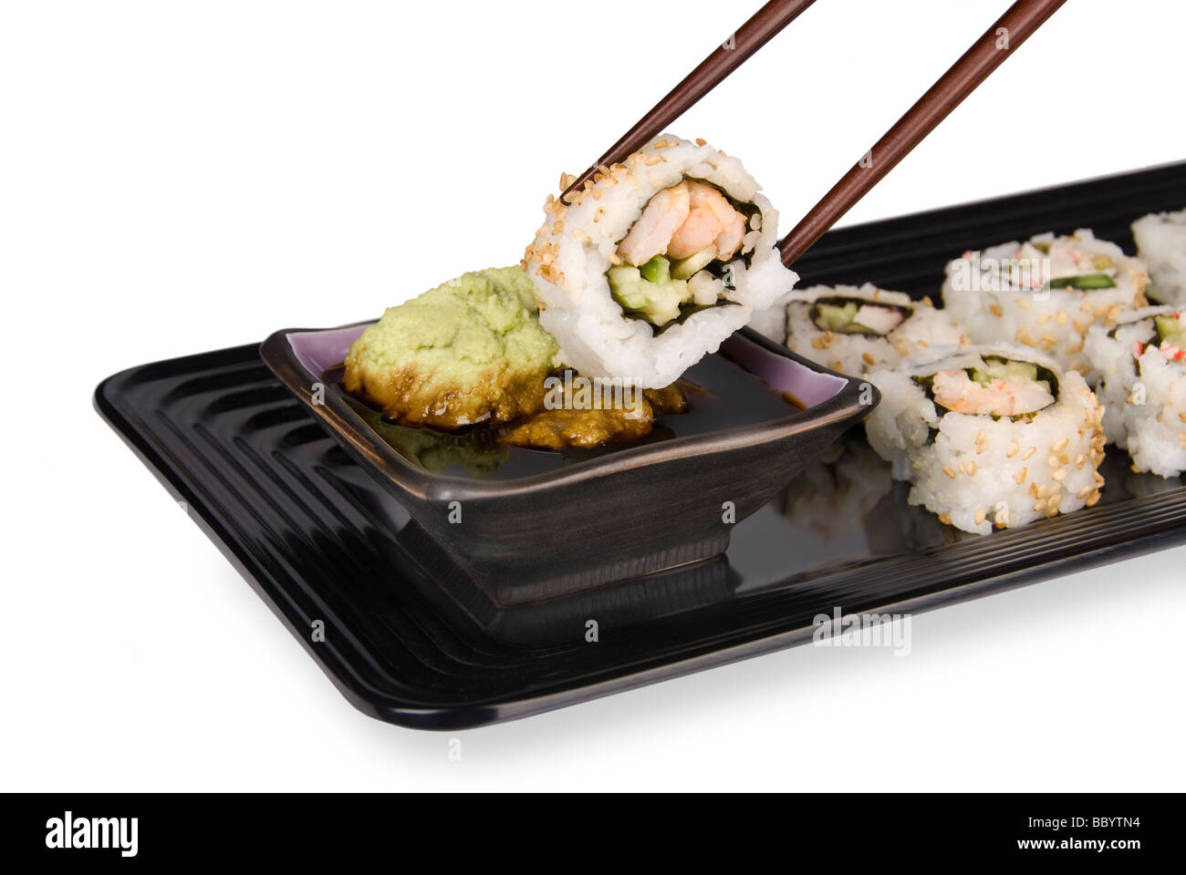 A fresh sushi roll of crab and fish being dipped into wasabi and soy sauce using chopsticks and an elegant serving tray Stock Photo