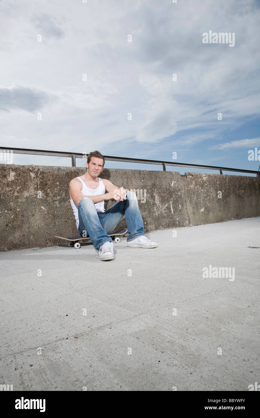 Skateboarder sitting in front of a wall, exhausted Stock Photo