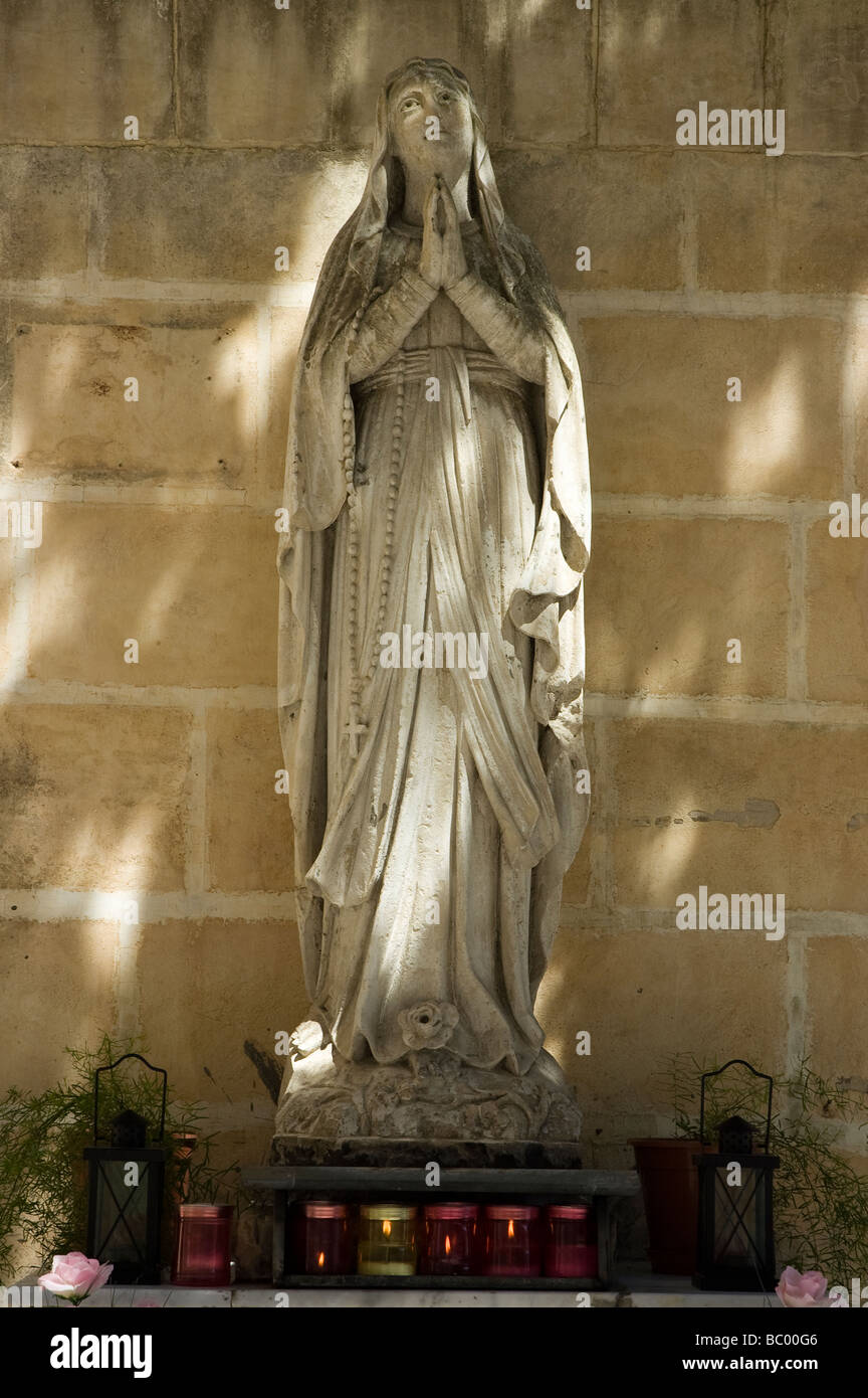 A statue of a Christian woman praying, with lit candles at the statue's base. Stock Photo
