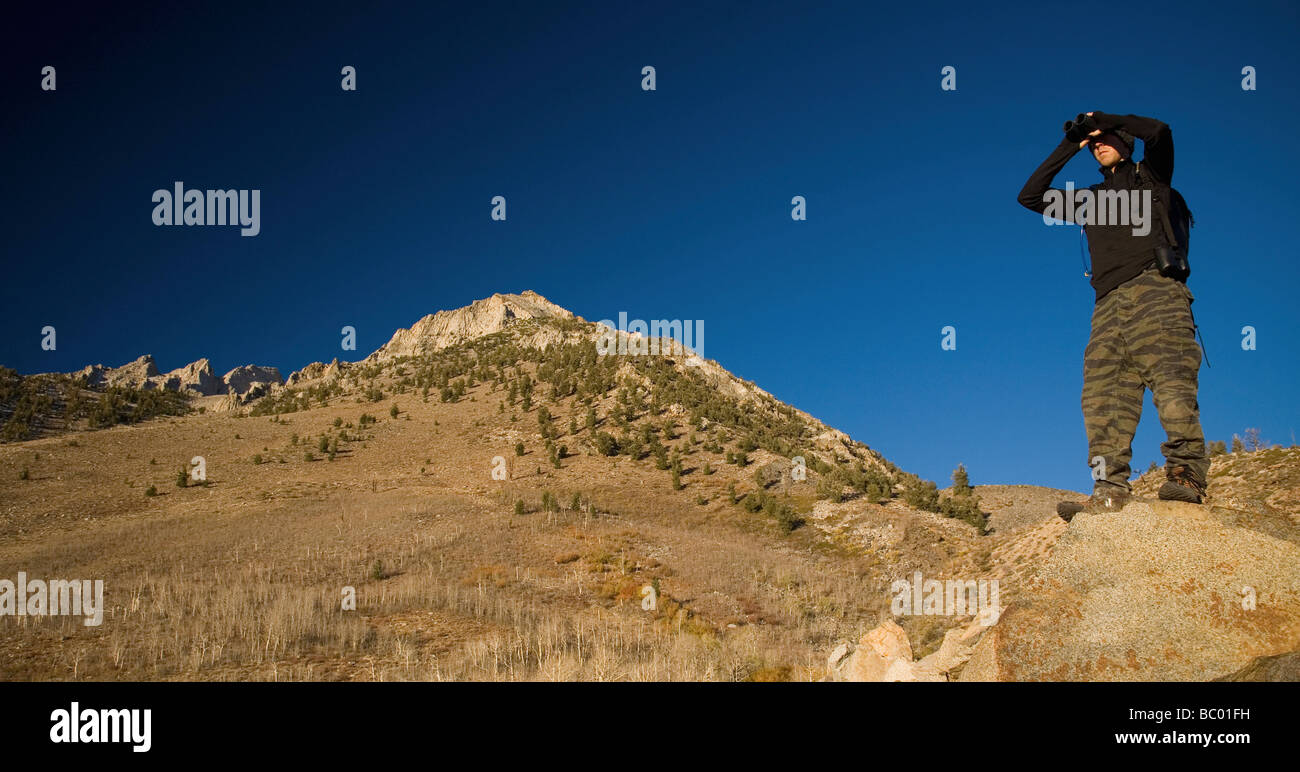 Hiker surveys his surroundings through binoculars. Stock Photo