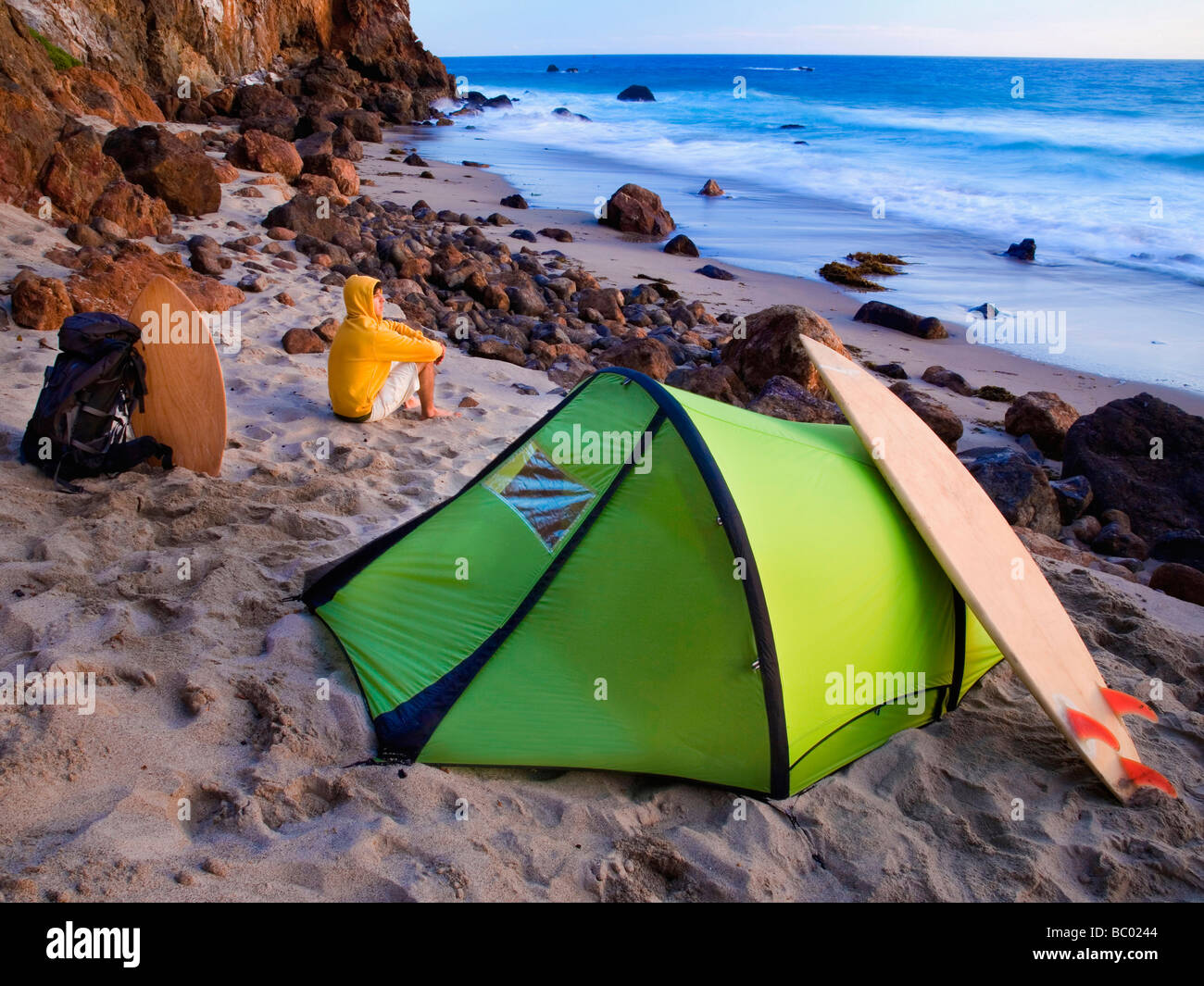 A young man camping on the beach waiting for surf. Stock Photo