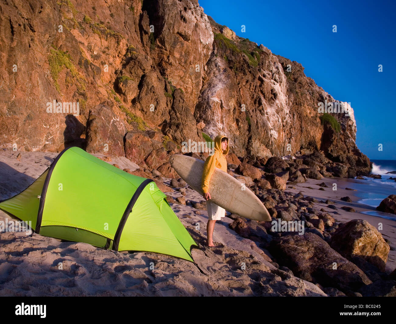 A young man camping on the beach waiting for surf. Stock Photo