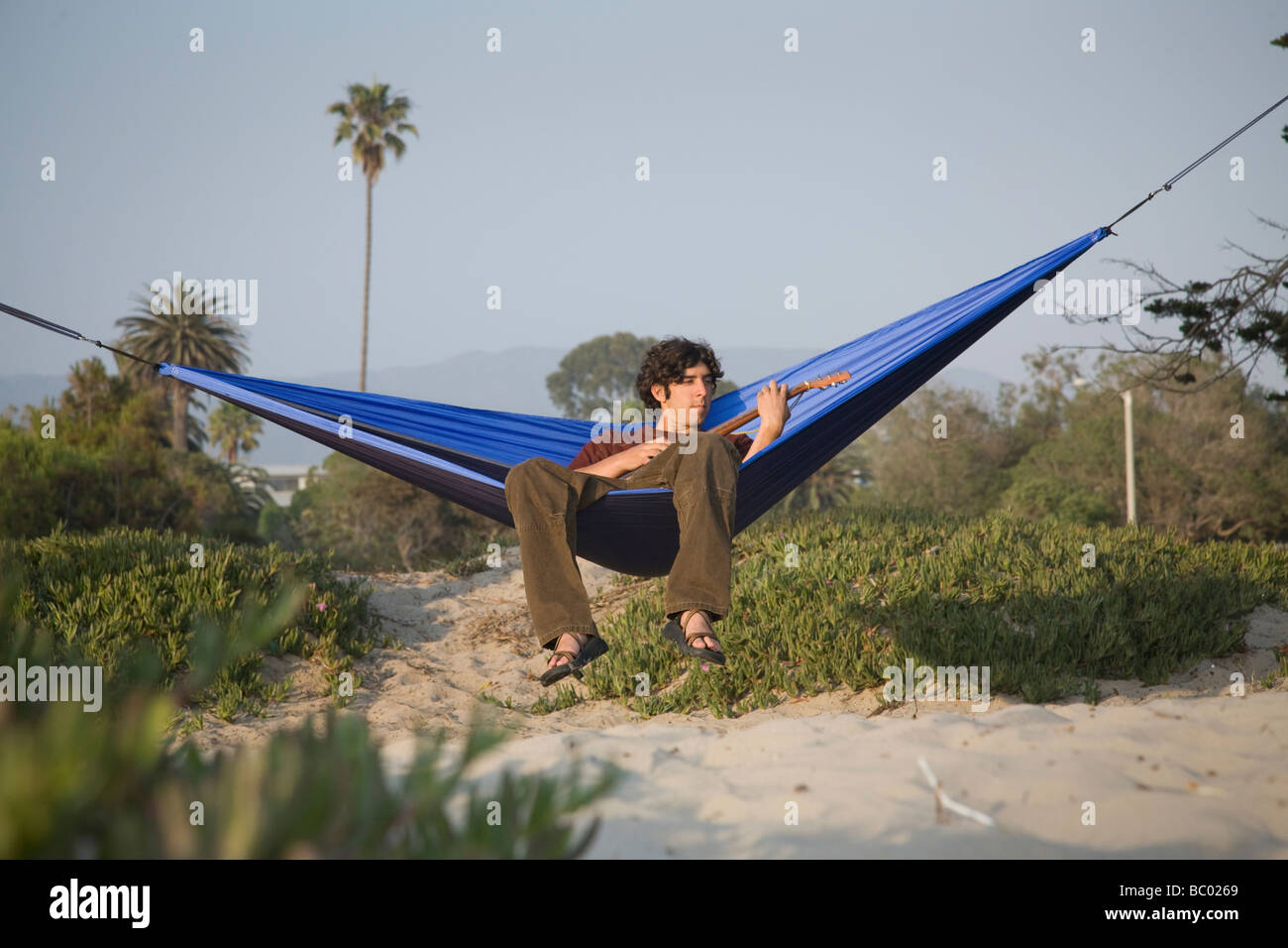A man relaxing and playing a guitar in a hammock on the beach. Stock Photo