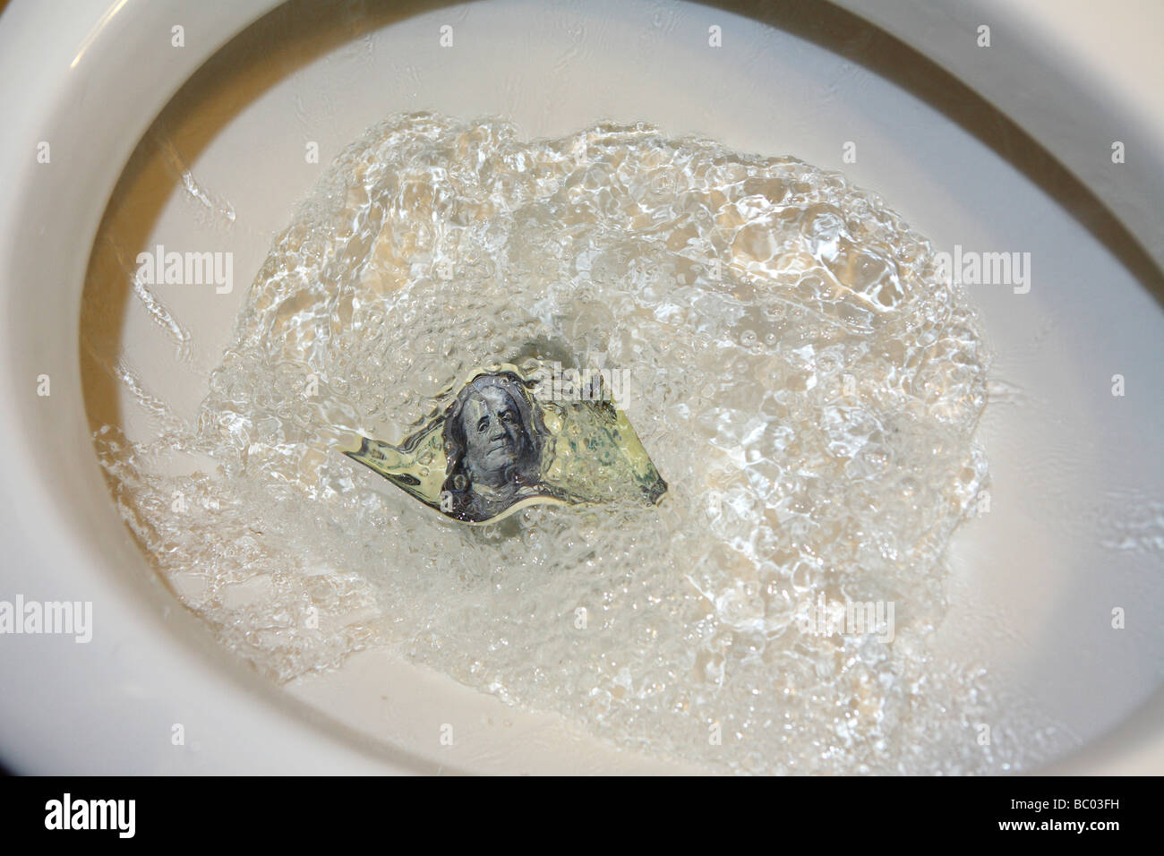 A one hundred dollar bill getting flushed down a toilet Stock Photo