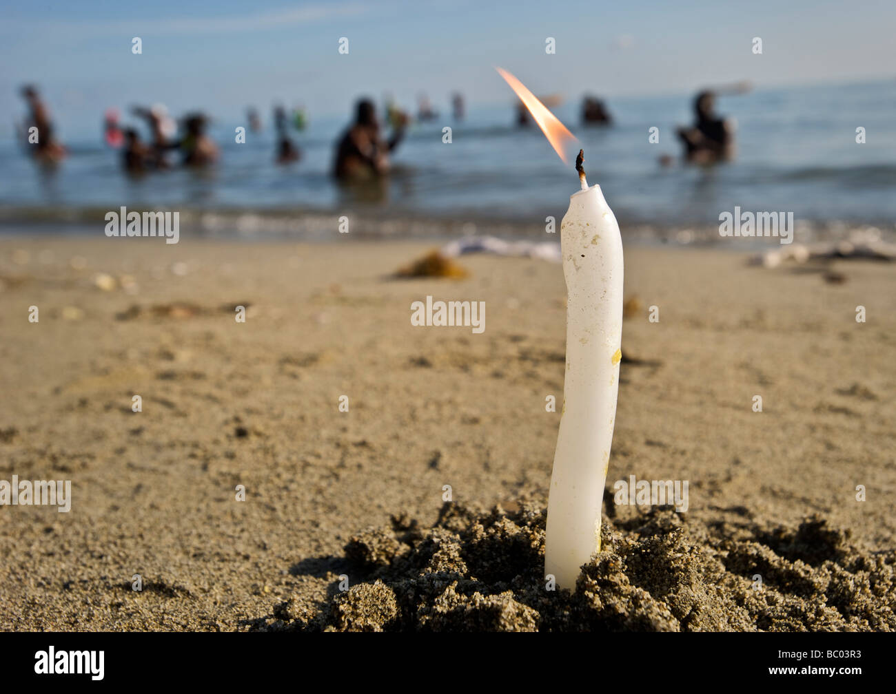 A candle burns in the sand as voodoo worshipers bathe in the ocean in