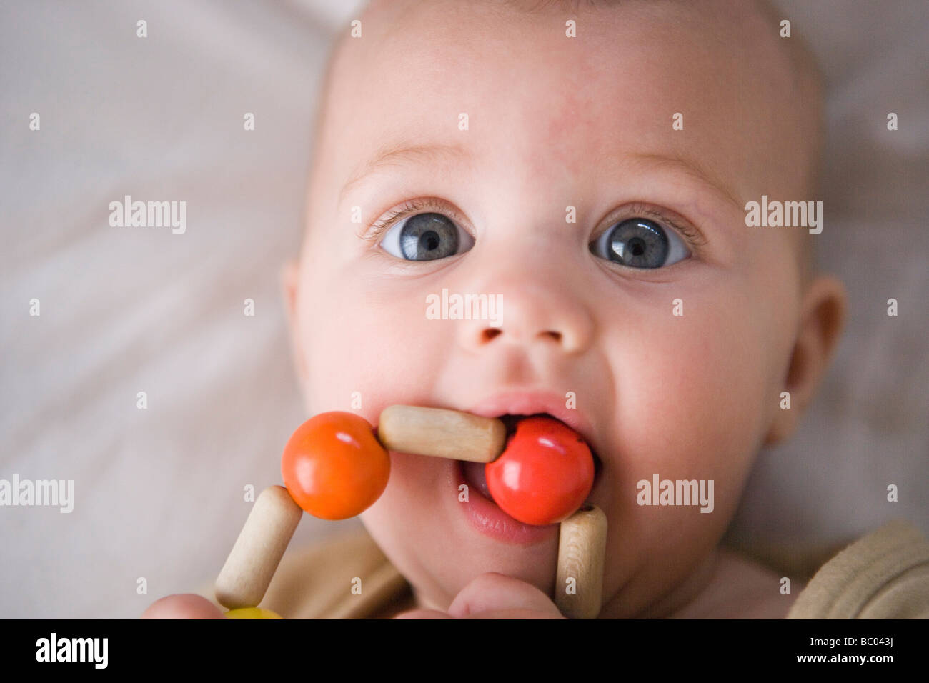 three month old baby girl grasping and mouthing a teething ring made of