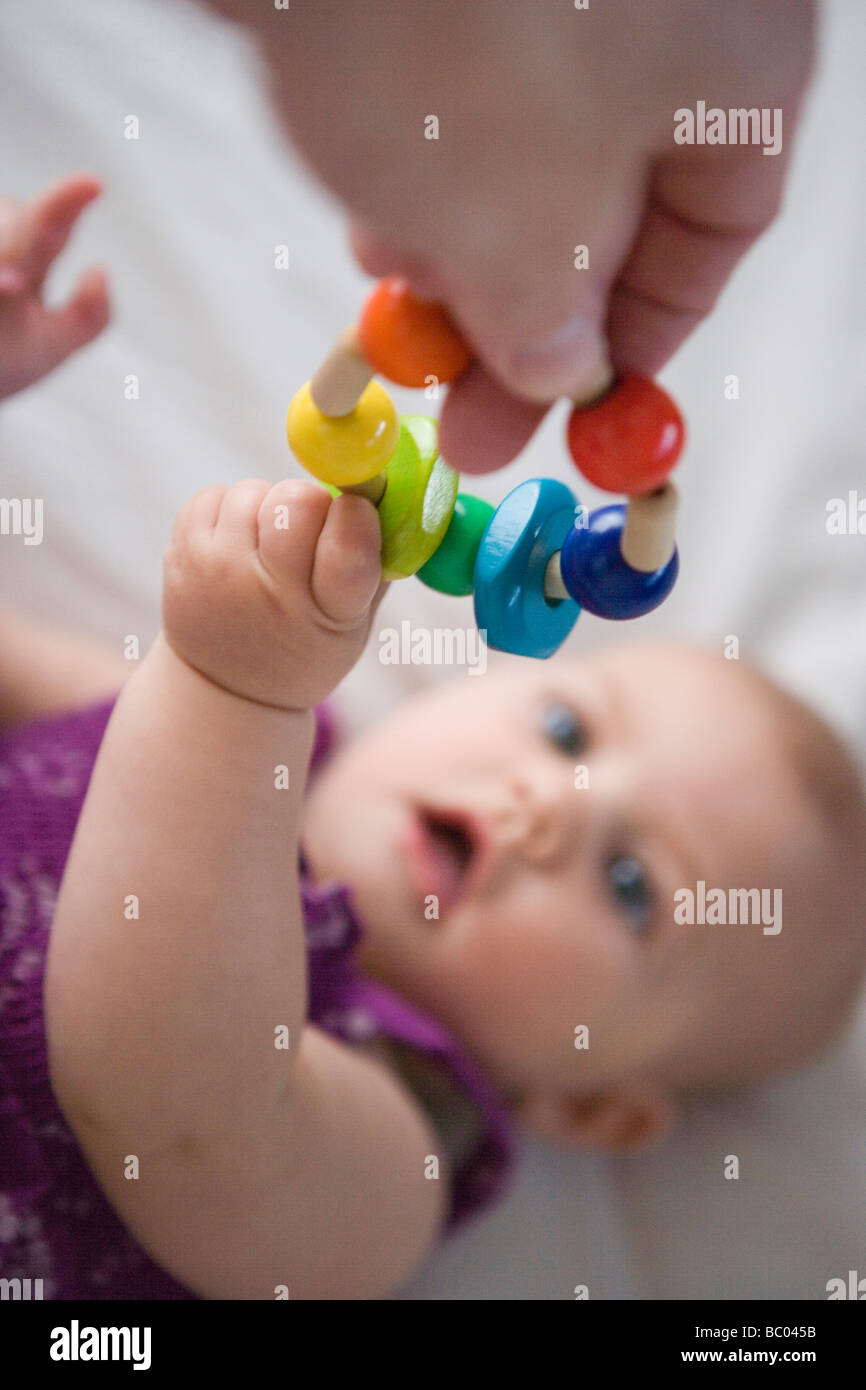 three month old baby girl reaching for a wooden teething toy Stock Photo