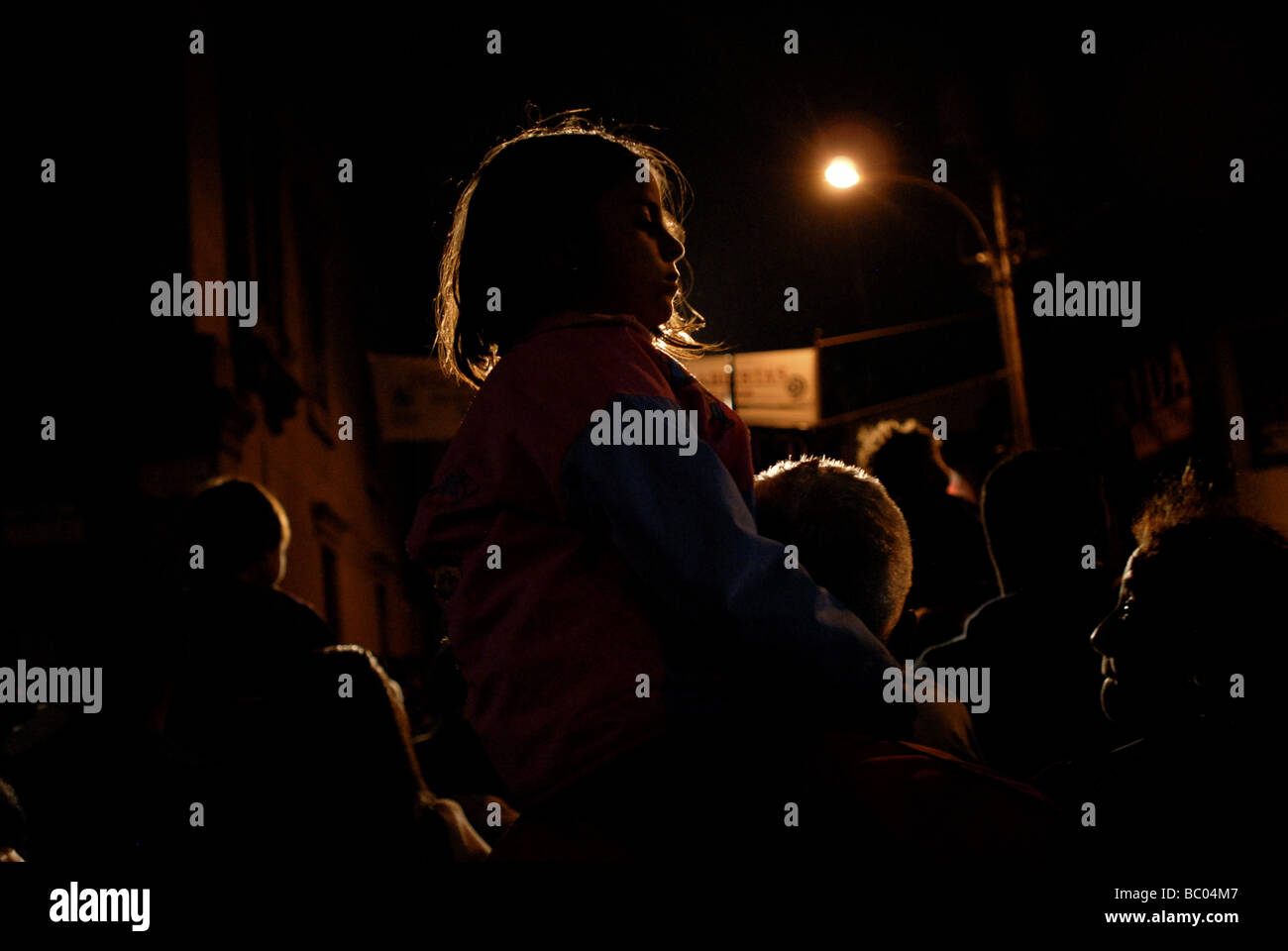 A young Catholic girl sits atop her parent's shoulders during a night religious procession to celebrate holy week in Merida, Ven Stock Photo