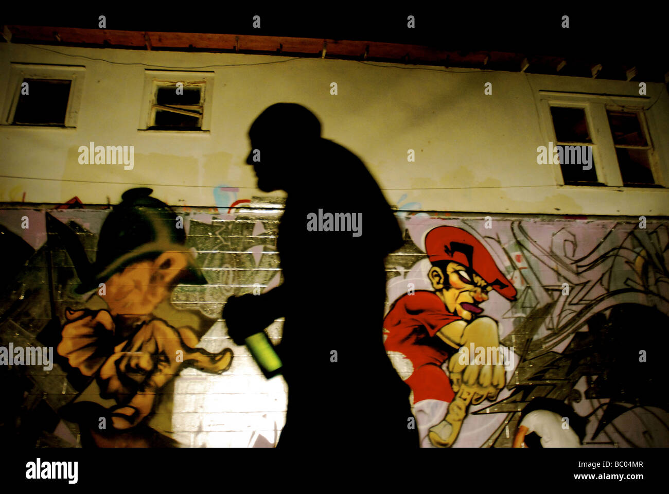 Silhouetted artist walks by graffiti wall in Austin, Texas. Stock Photo