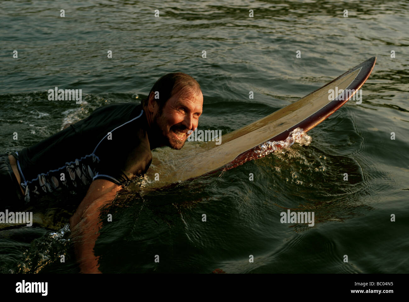 A smiling, middle-aged man paddles a surfboard in Austin, Texas. Stock Photo