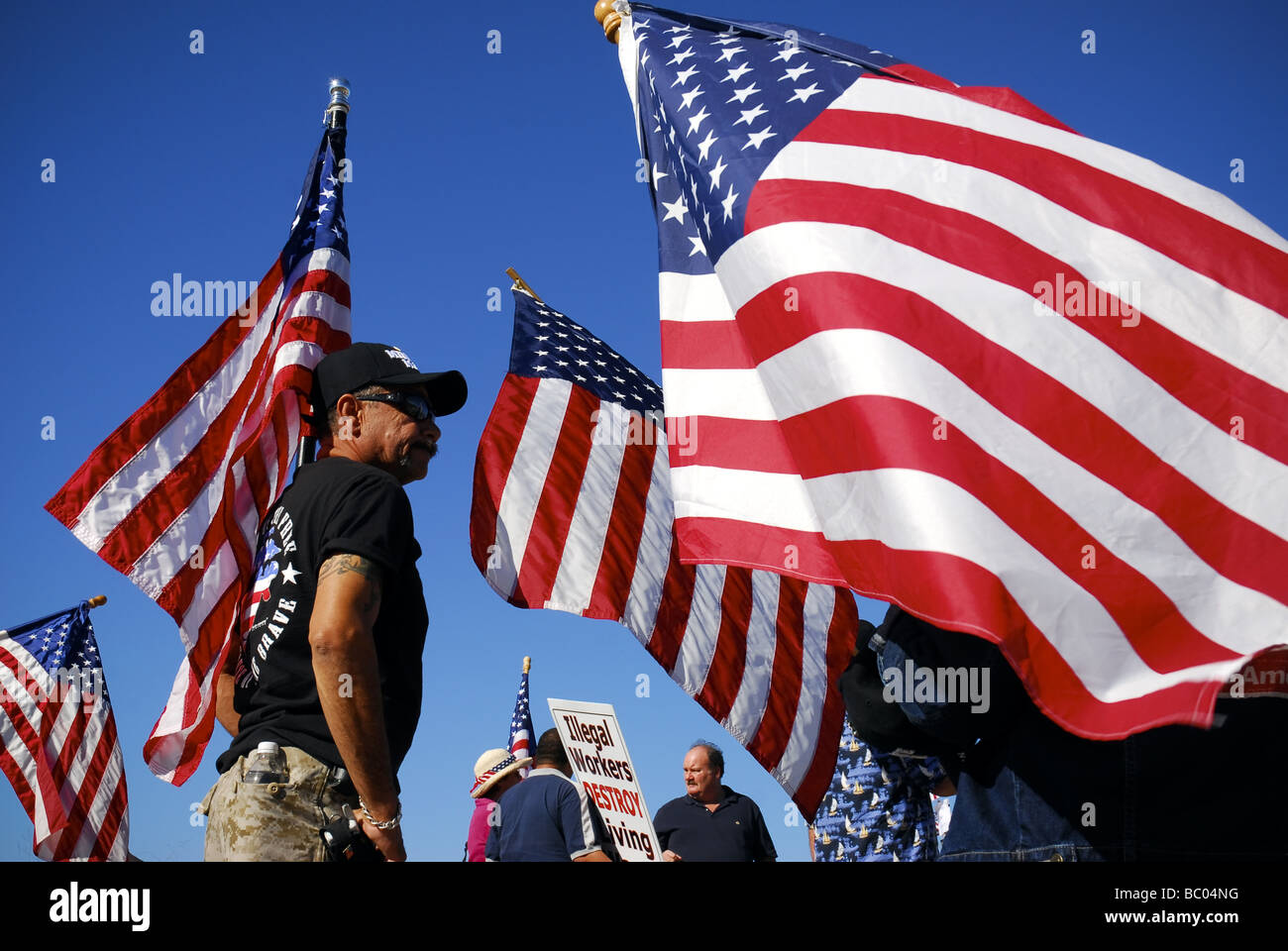 An immigration activist stands surrounded by waving American flags at a Minute Men ralley in San Diego, California. Stock Photo