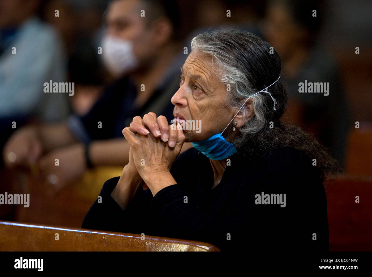 A woman wears a mask as a precaution against swine flu prays in Mexico City's Metropolitan Cathedral. Stock Photo