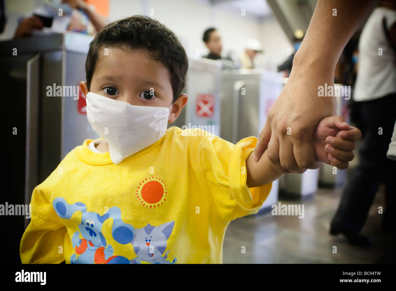 A small kid wearing a mask is held by his mother's hand at a metro station in Mexico City, DF, Mexico. Stock Photo