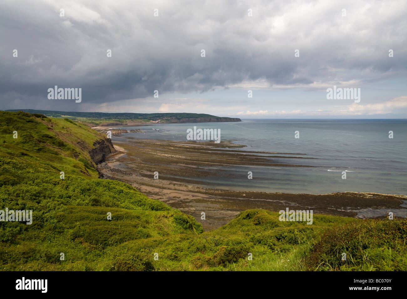 Cliff top view with stormy sky looking towards Robin Hoods Bay from Peak Alum Works Ravenscar North Yorkshire England Stock Photo