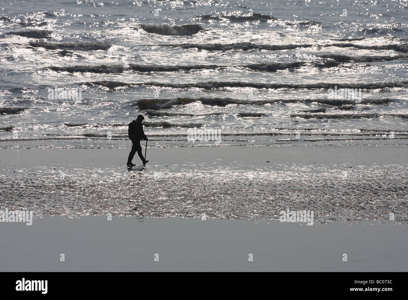 Man walking on wet beach in silhouette. Stock Photo