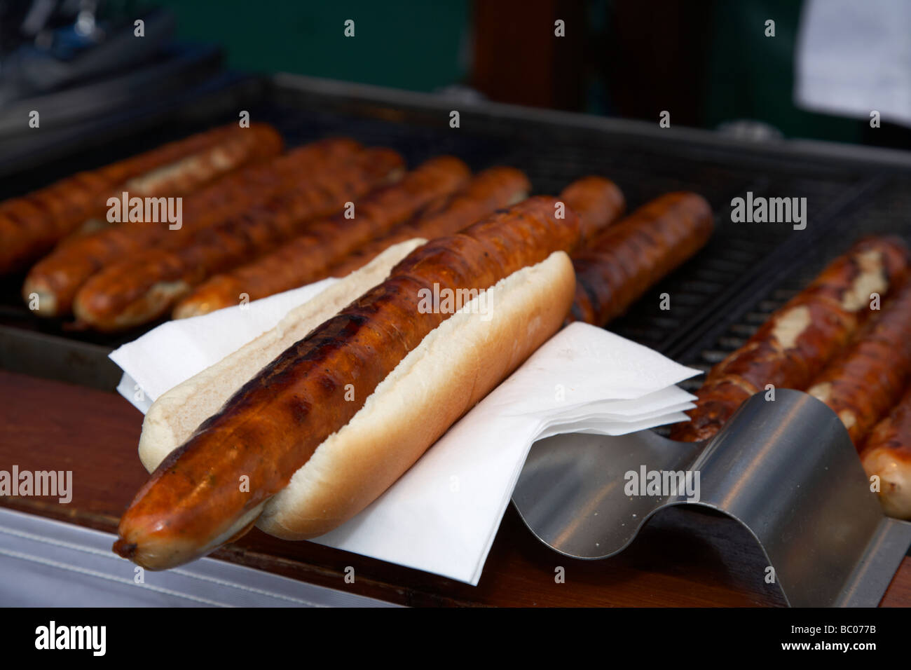 bratwurst in bread roll bap on napkin with german sausages on grill on sale at an outdoor market in the uk Stock Photo