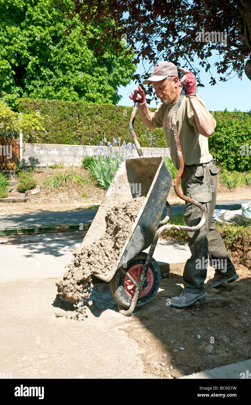 Building worker pouring concrete from wheelbarrow for vehicle hard