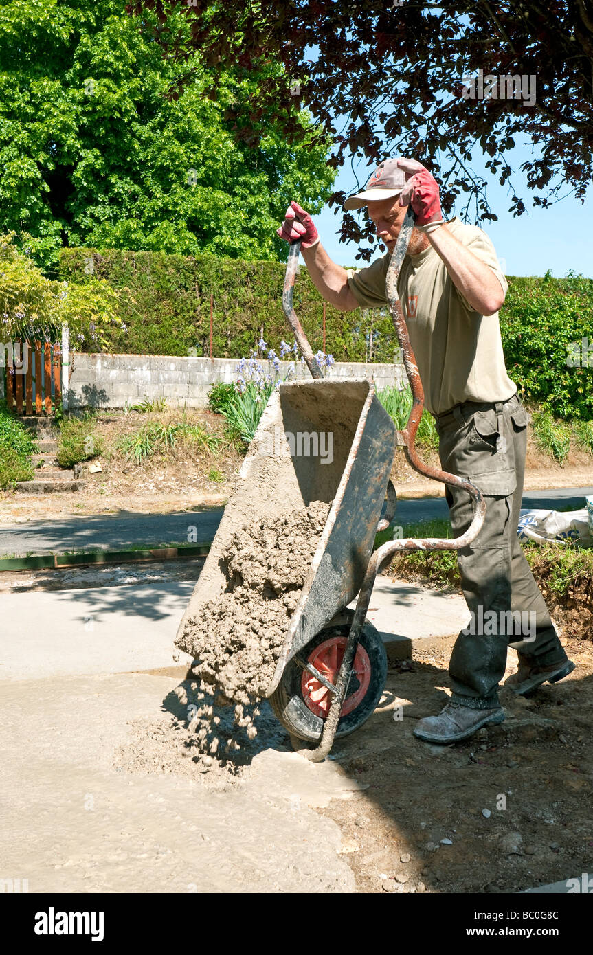 Building worker pouring concrete from wheelbarrow for vehicle hard standing. Stock Photo