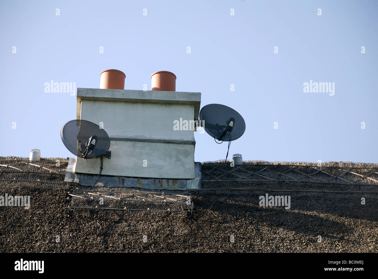 Two television satellite dishes on the chimney of a thatched cottage, Devon, UK Stock Photo