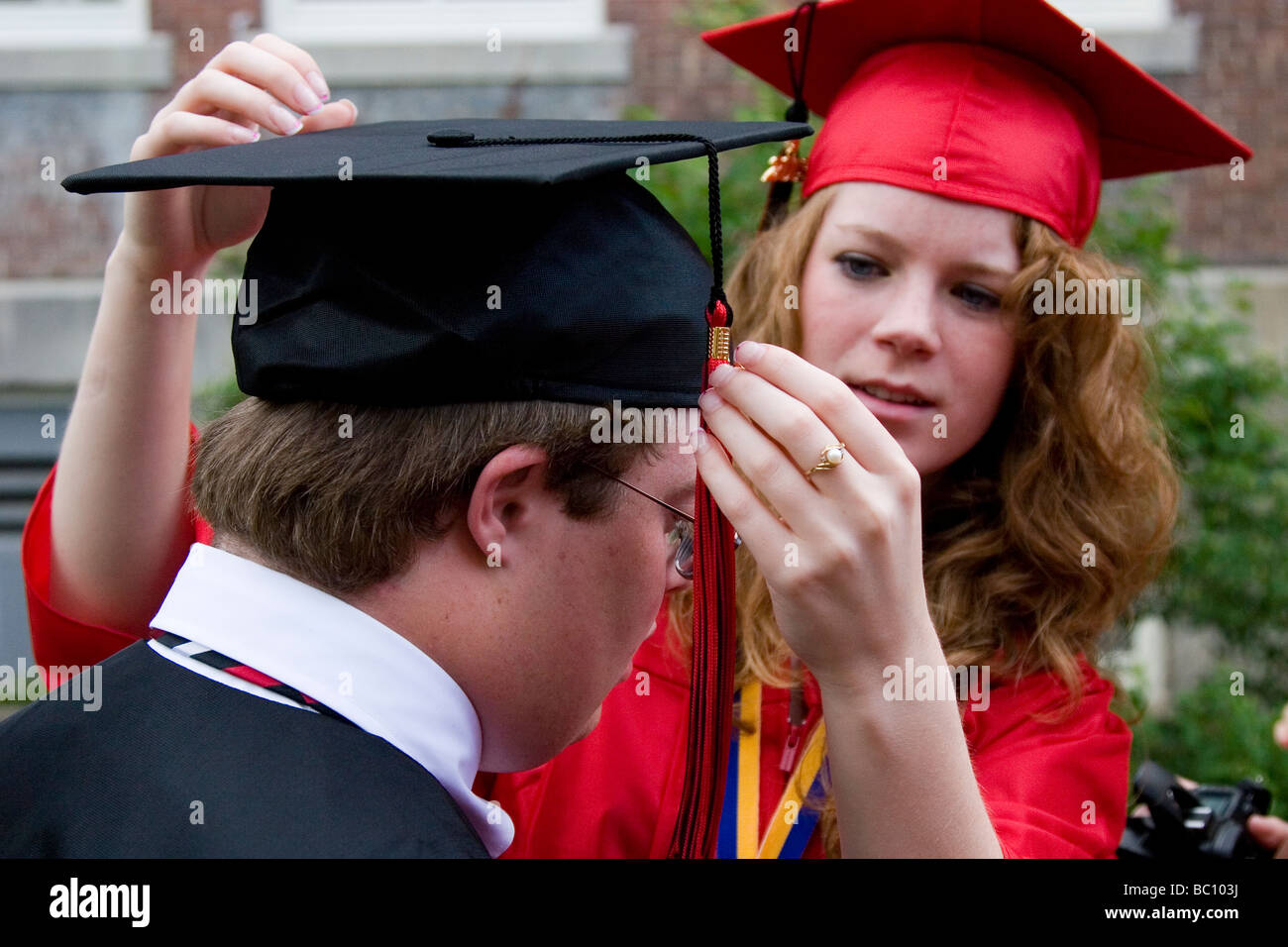 Female graduate helps another with his cap and tassel Stock Photo - Alamy