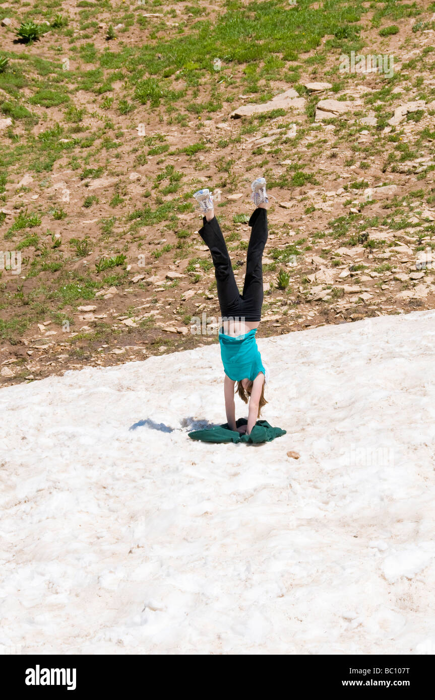 Button Handstand A young girl does a handstand in the snow during the summer on top of ...