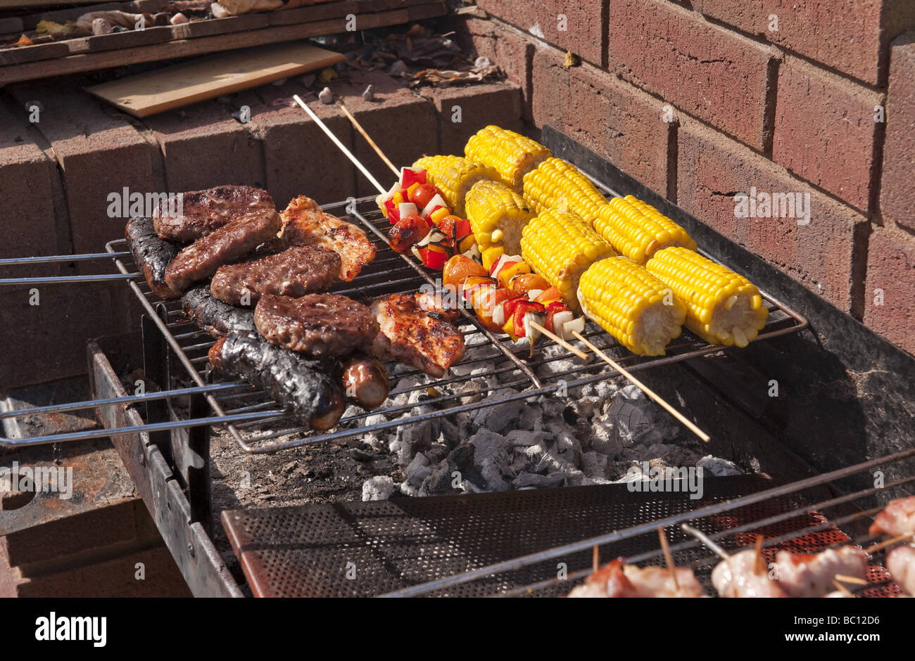 Close-up of sausages, burgers and corn and kebabs being cooked outside in the open air on a barbeque (bbq) in summer Stock Photo